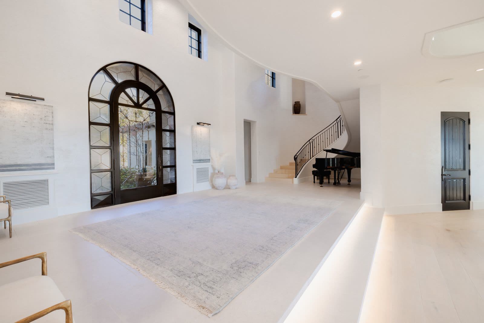 Double-height entry hall with an arched window and a grand piano