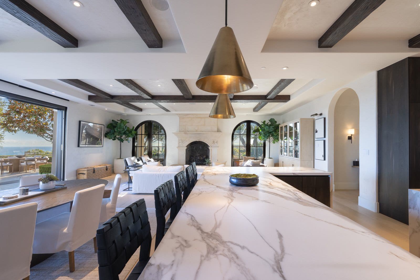 Open kitchen and dining room with a marble island, dark timber beams and an ocean view