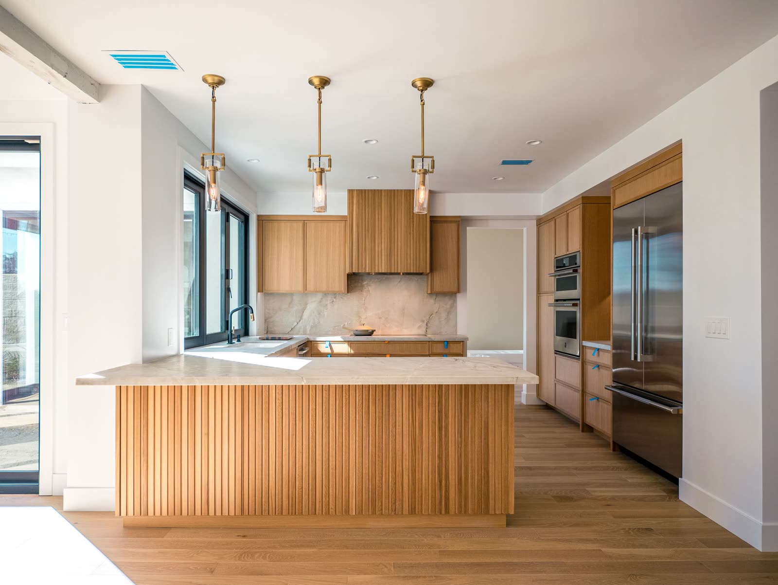 Kitchen with a fluted oak island, marble counters and integrated appliances