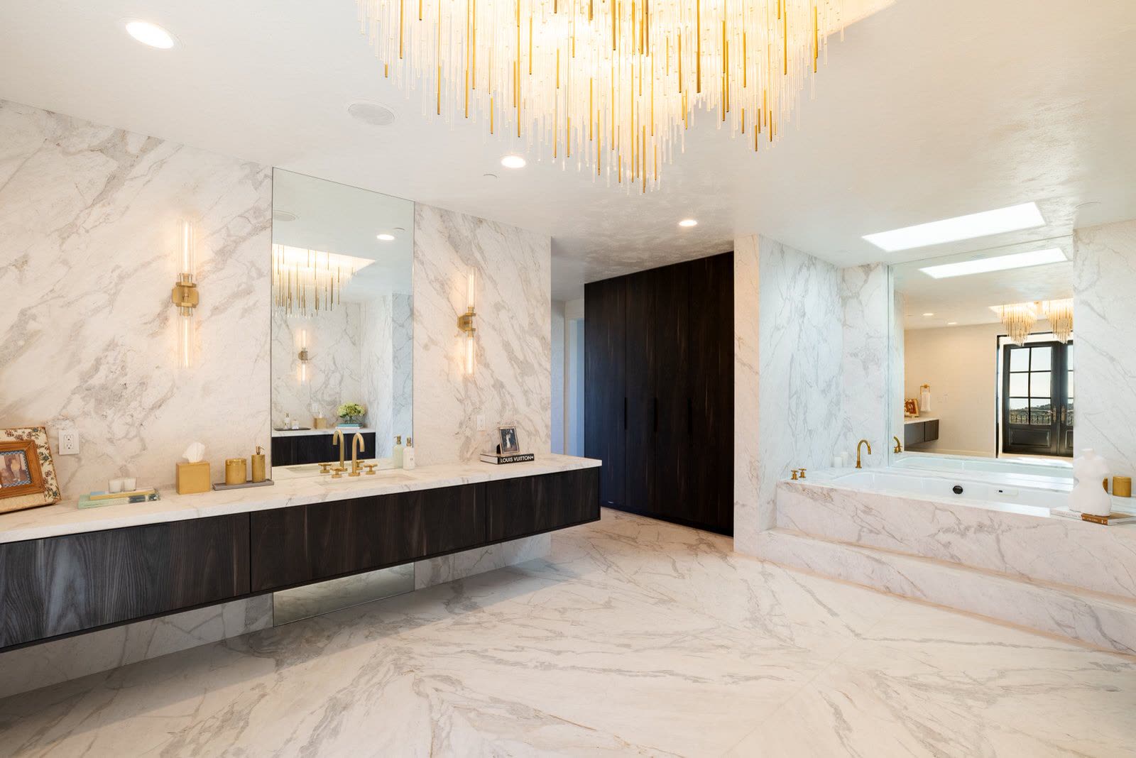 Primary bathroom in book-matched marble with a linear brass chandelier